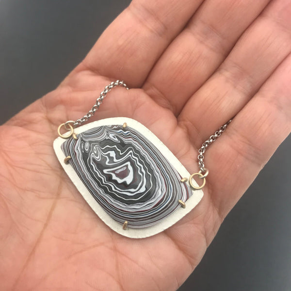 Fordite Pendant Silver and Gold Necklace No 2 by tkmetalarts, sterling silver setting with 18k gold prongs, comes on an 20 to 22 inch chain, multicolor pattern. Shown on hand for scale.